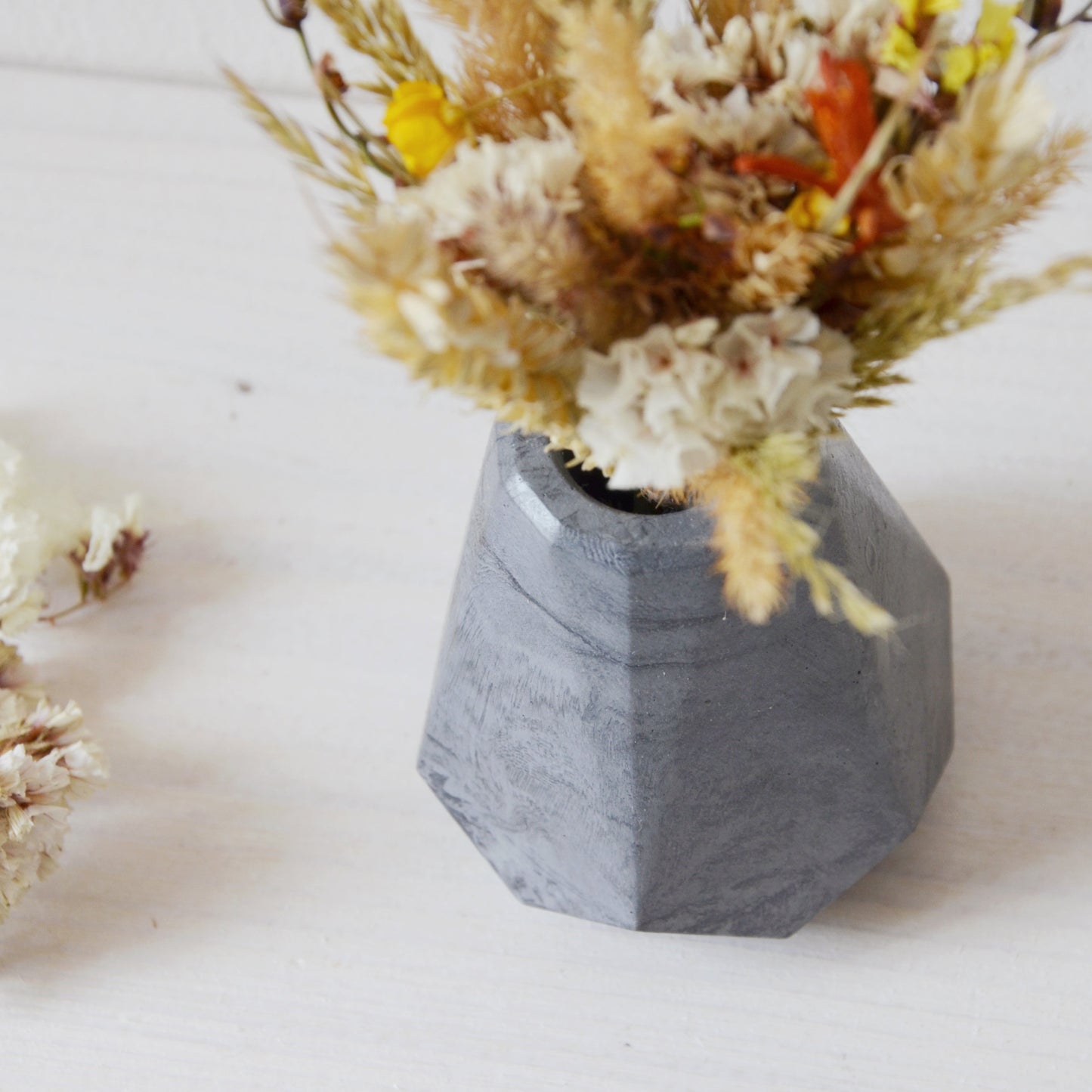 concrete vase with dried flowers Květina sušená v betonové vázičce - tmavě šedá diamant. Close up. Point of view from above