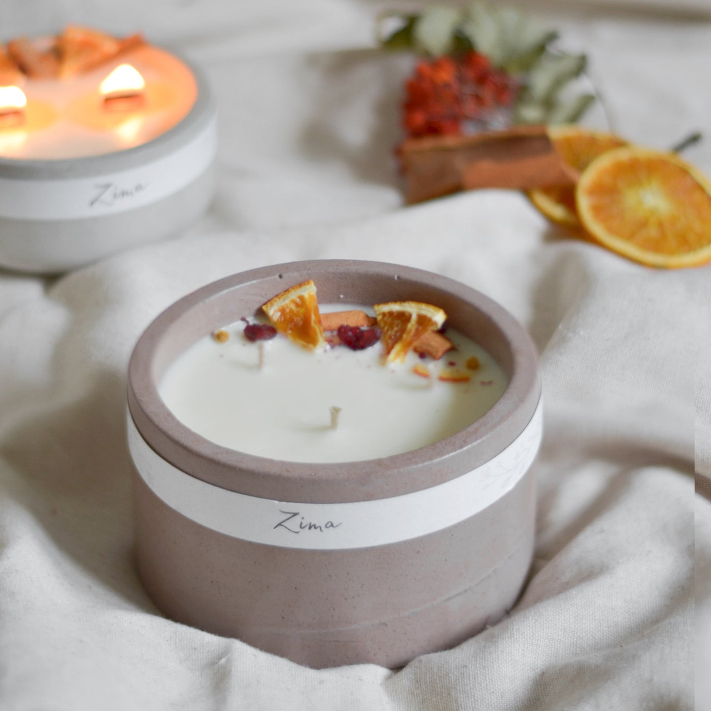 Sójová svicka v betonu se tremi knoty s vuni zimy. Zdobena zimnim korenim a pomerancem. V pozadi svicka hori