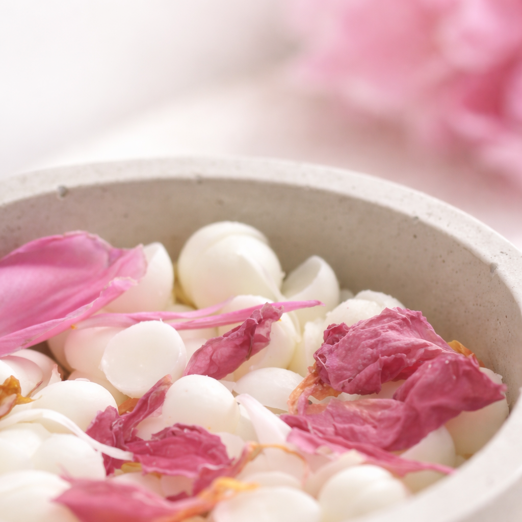 Makro detail přírodních vonných vosků s pivoňkovými lístky na světlém, jemně rozostřeném pozadí