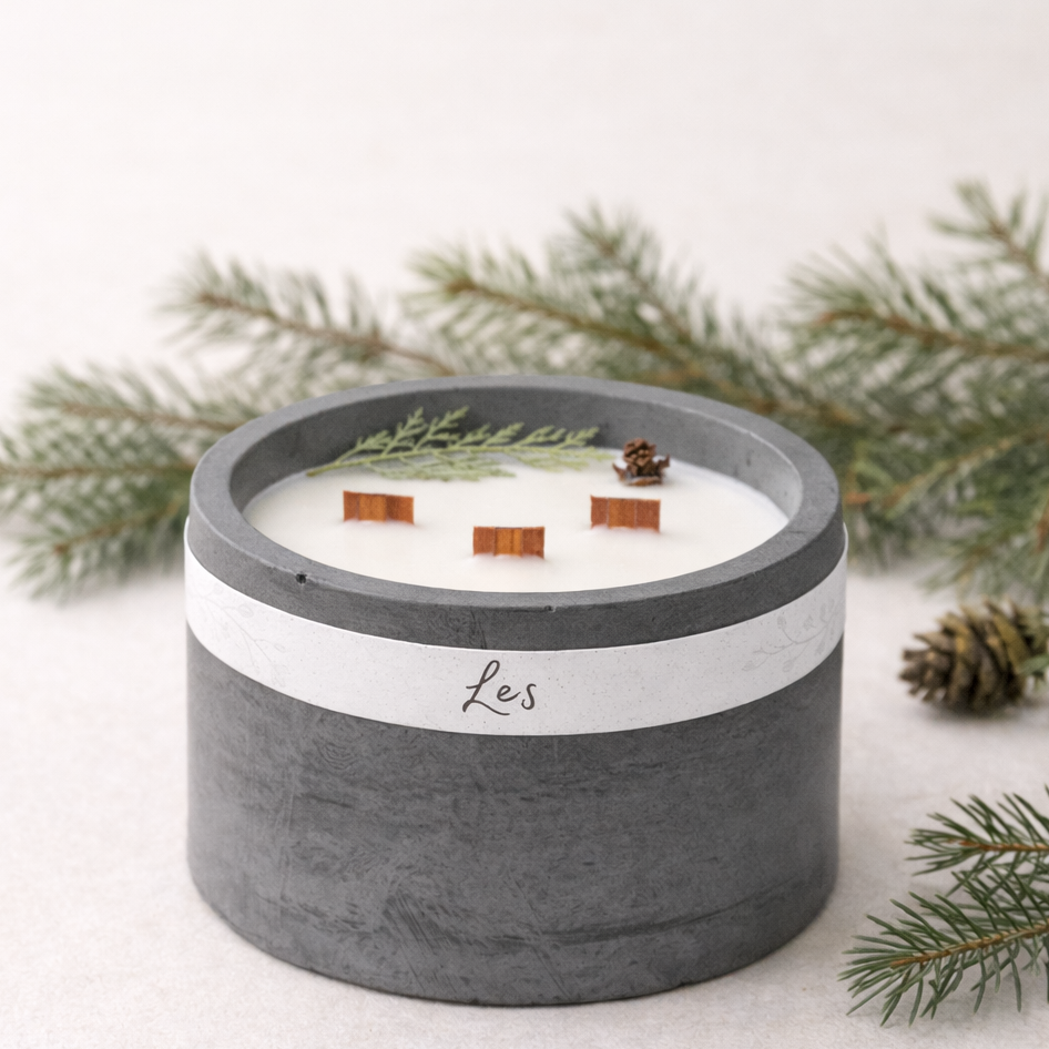 Sójová svíčka Les v tmavě šedém betonovém obalu s třemi dřevěnými knoty, aranžovaná s lesními větvičkami na světlém minimalistickém pozadí.