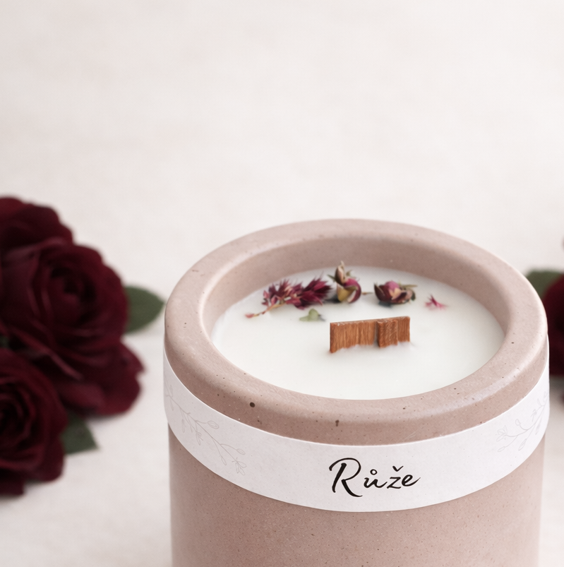 Sójová svíčka s vůní růže v starorůžovém betonovém kalíšku, ruční výroba, doplněná tmavě vínovými růžemi na světlém přírodním pozadí.