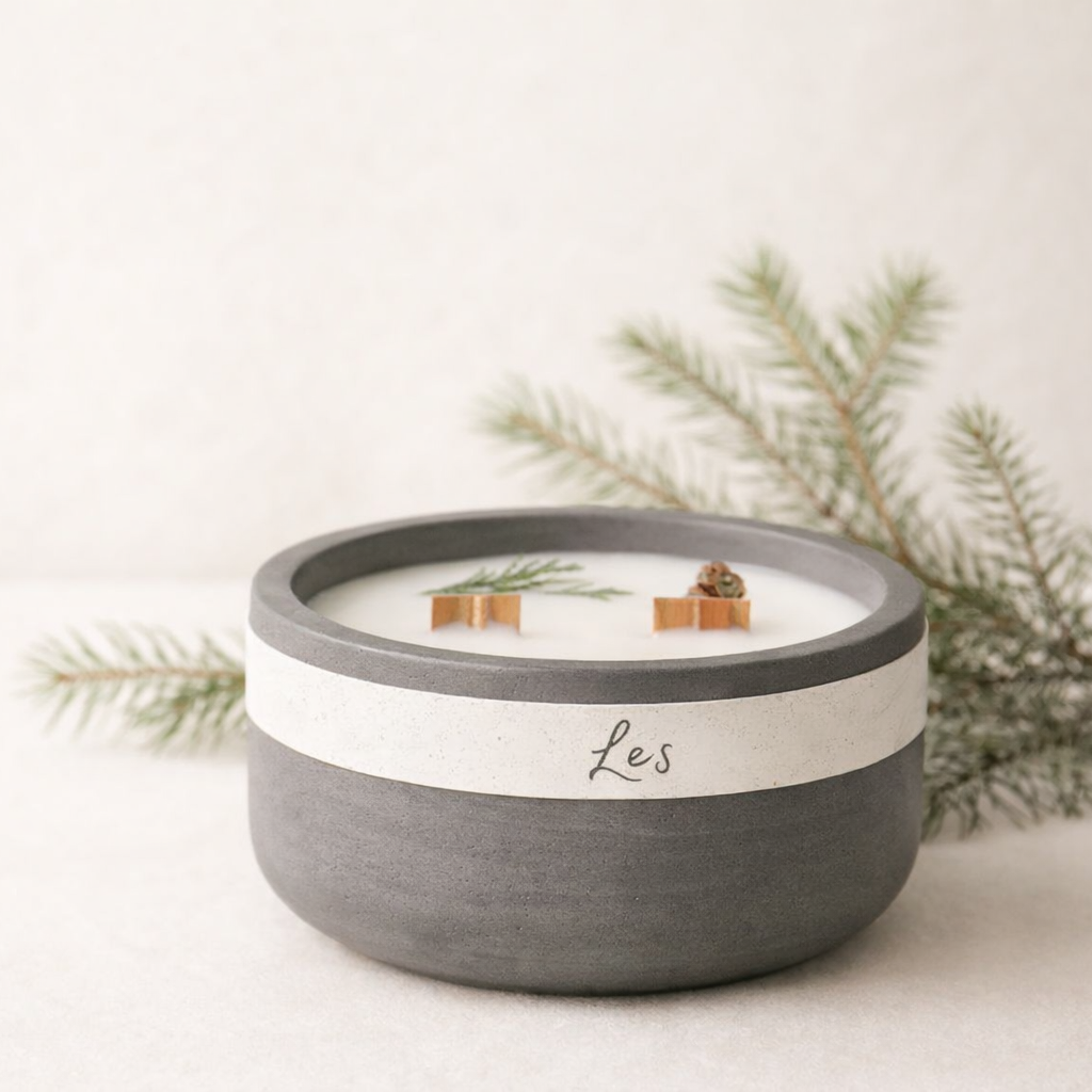 Ručně vyráběná sójová svíčka Les v šedé keramické misce na světlém krémovém pozadí, doplněná jemnými lesními větvičkami.