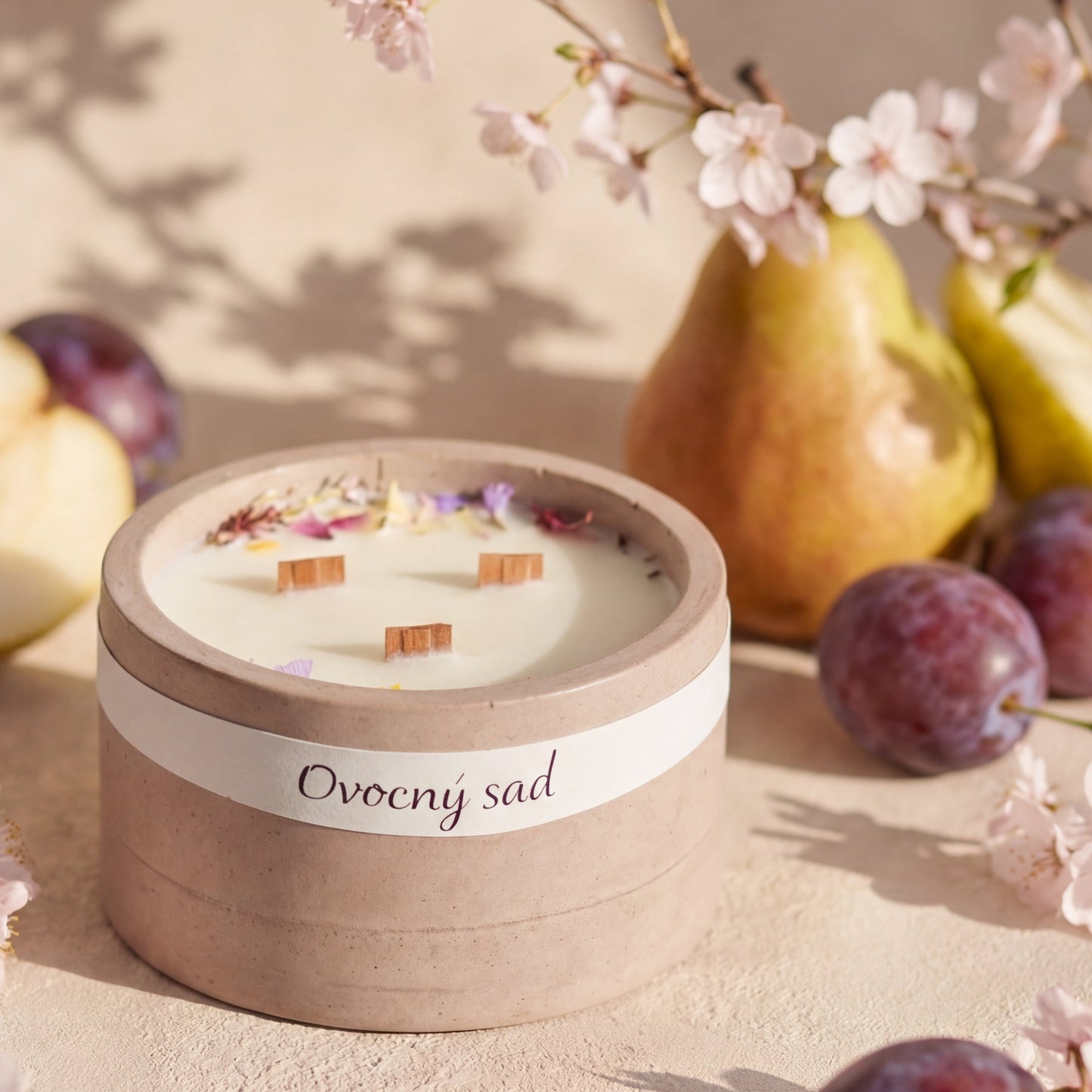 Ručně vyráběná svíčka v keramické misce s květy na vosku, obklopená hruškou, švestkou a rozkvetlými třešňovými květy.