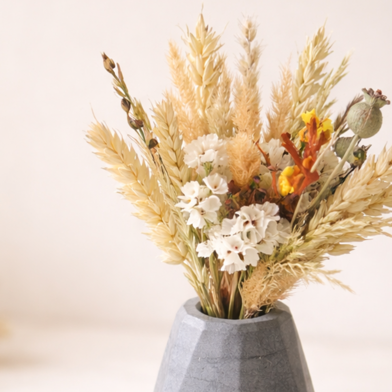 kvetina susena s vazickou v tmave sede barve ve tvaru diamantu na svetlem pozadi zdobena naboku susenymi kvetinami