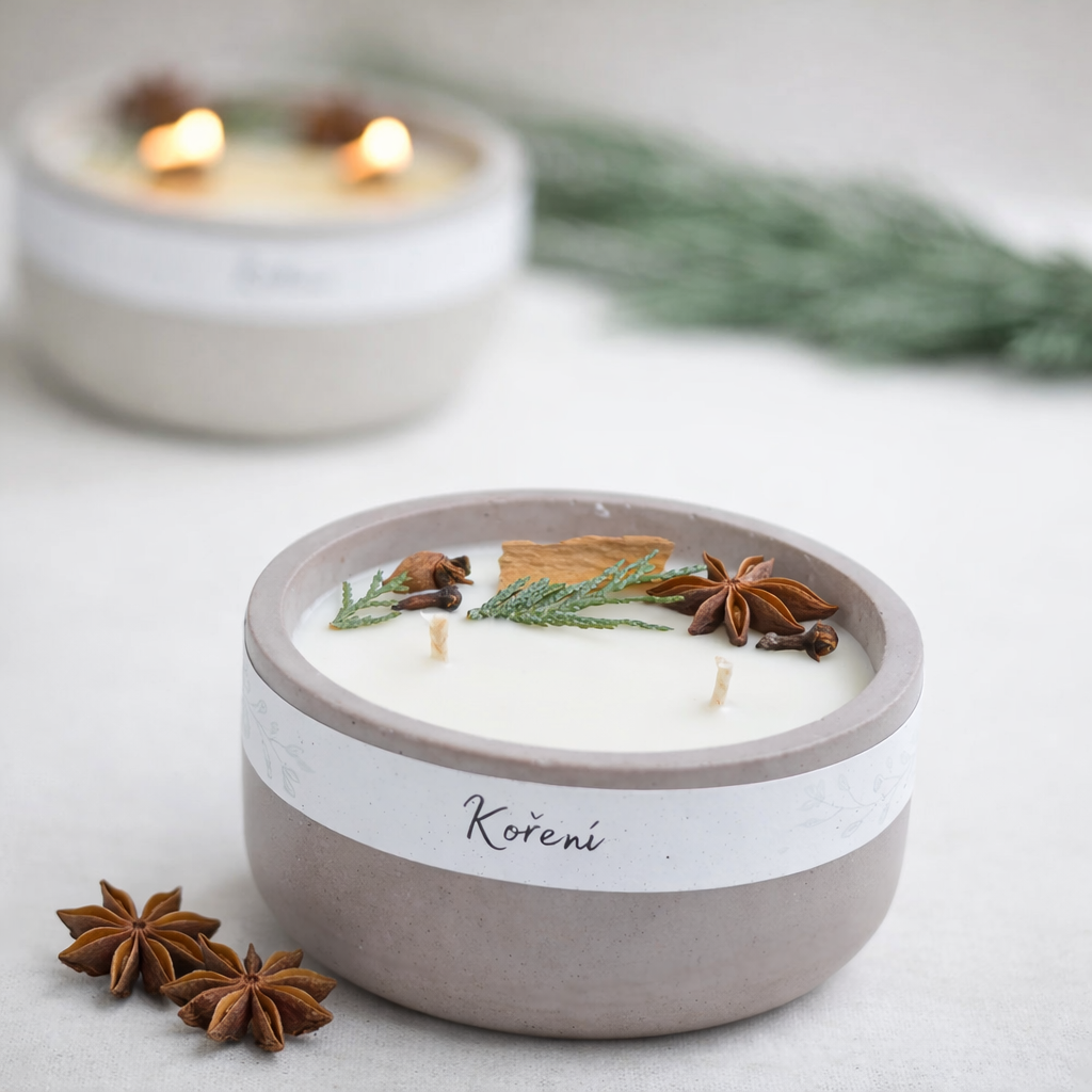 Ručně vyráběná vonná svíčka Koření v betonové misce, s krémovým voskem, bavlněnými knoty a dekorací z badyánu, skořice a jehličí na světlém pozadí.“