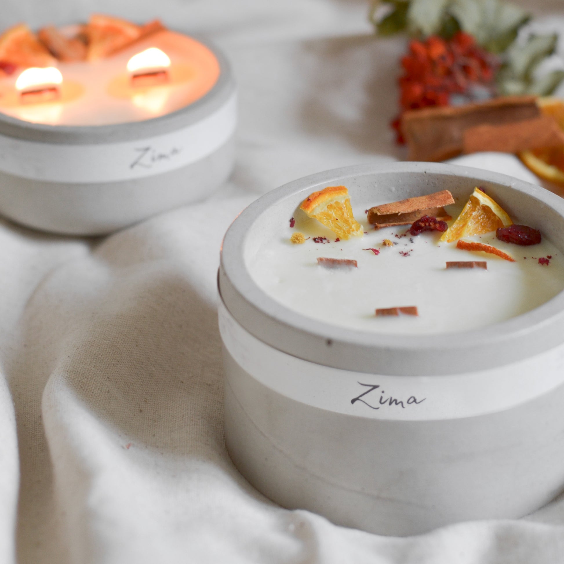 Sójová svicka ve svetle sedem betonu se tremi drvenymi knoty s vuni zimy. Zdobena zimnim korenim a pomerancem. V pozadi svicka hori