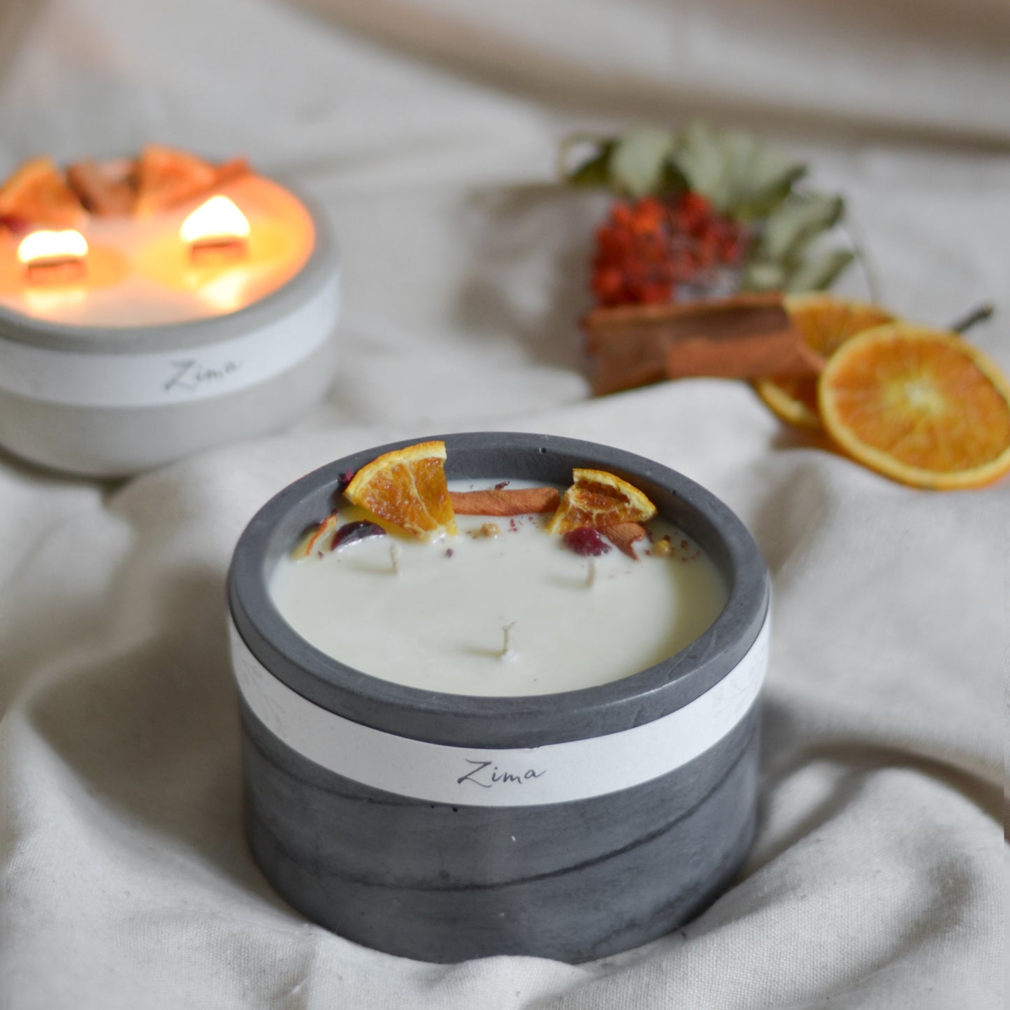 Sójová svicka v betonu se tremi bavlnenymi  knoty s vuni zimy. Zdobena zimnim korenim a pomerancem. V pozadi svicka hori