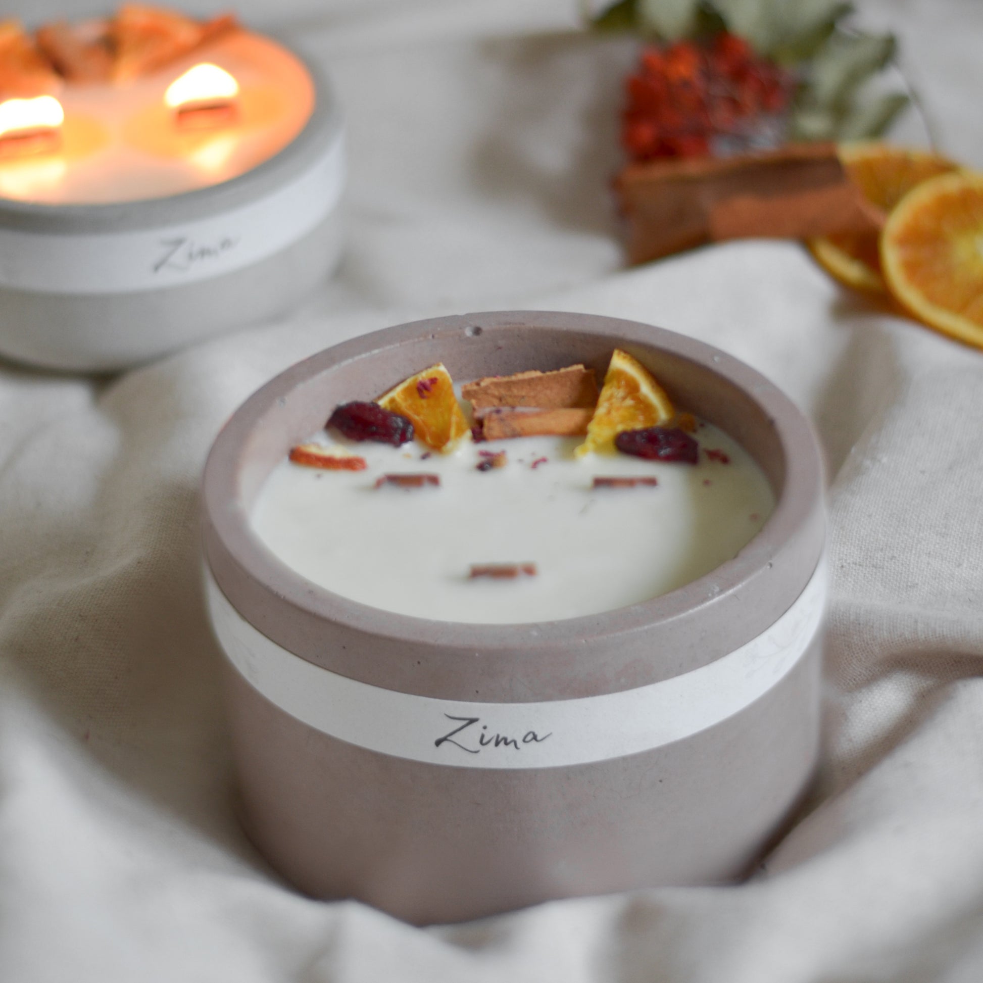 Sójová svicka v betonu se tremi drevenymi knoty s vuni zimy. Zdobena zimnim korenim a pomerancem. V pozadi svicka hori