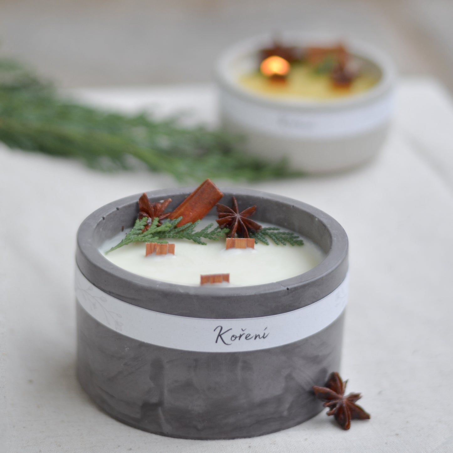 Ručně vyráběná vonná svíčka Koření ve tmavě  šedé betonové mističce se třemi knoty, ozdobená skořicí, badyánem a větvičkami jehličí.
