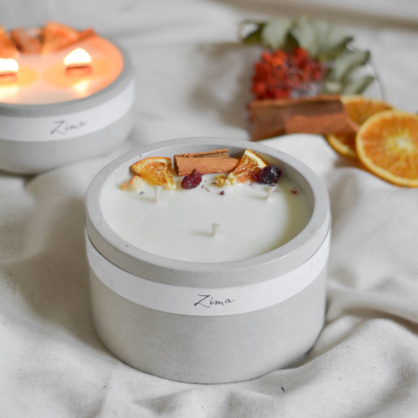 Sójová svicka v betonu se tremi bavlnenymi knoty  s vuni zimy. Zdobena zimnim korenim a pomerancem. V pozadi svicka hori