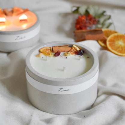 Sójová svicka v betonu se tremi bavlnenymi knoty  s vuni zimy. Zdobena zimnim korenim a pomerancem. V pozadi svicka hori