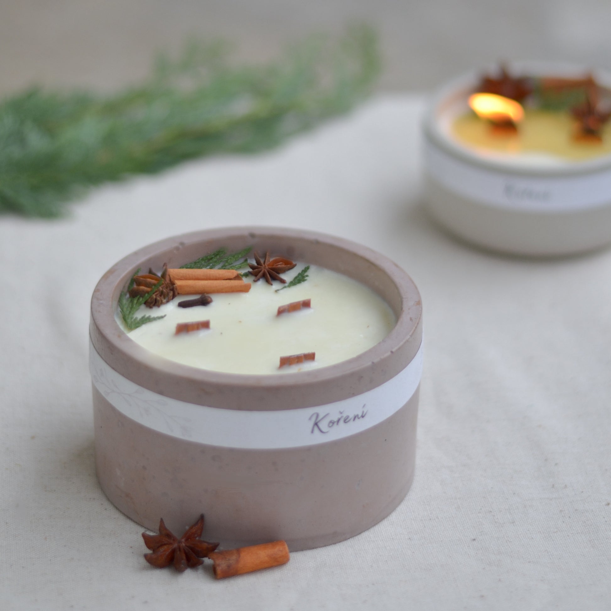 Ručně vyráběná vonná svíčka Koření ve starorůžové betonové mističce se třemi knoty, ozdobená skořicí, badyánem a větvičkami jehličí.