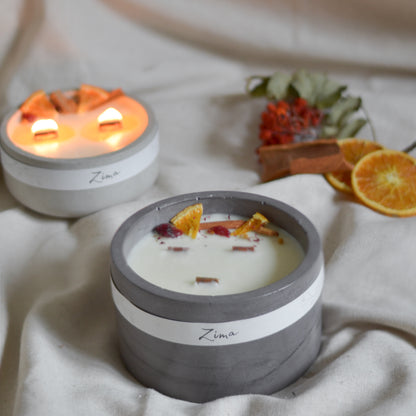 Sójová svicka v betonu se tremi drevenymi knoty s vuni zimy. Zdobena zimnim korenim a pomerancem. V pozadi svicka hori