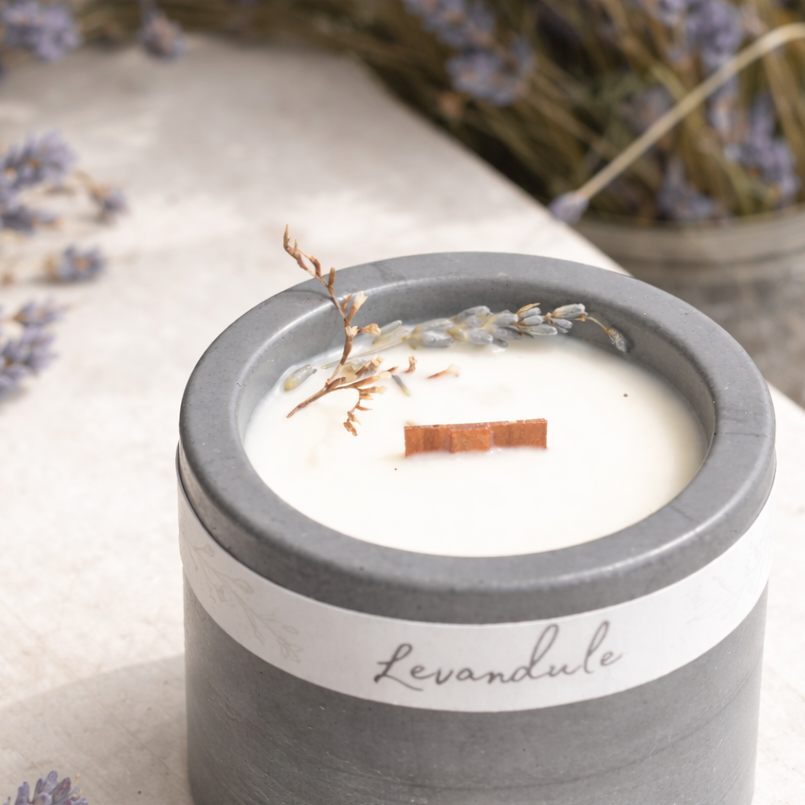 Detail sojové svíčky s dřevěným knotem a sušenou levandulí v tmavém betonovém kalíšku, foceno v měkkém přirozeném světle.