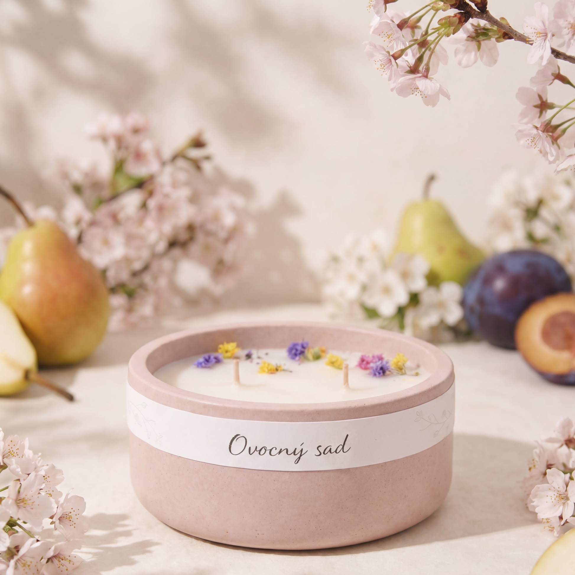 Pastelově růžová vonná svíčka v betonove nádobě s nápisem „Ovocný sad“, zdobená sušenými květy na povrchu vosku.