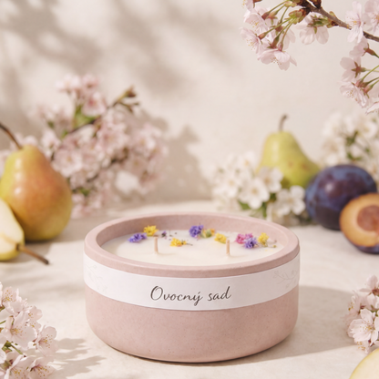 Pastelově růžová vonná svíčka v betonove nádobě s nápisem „Ovocný sad“, zdobená sušenými květy na povrchu vosku.