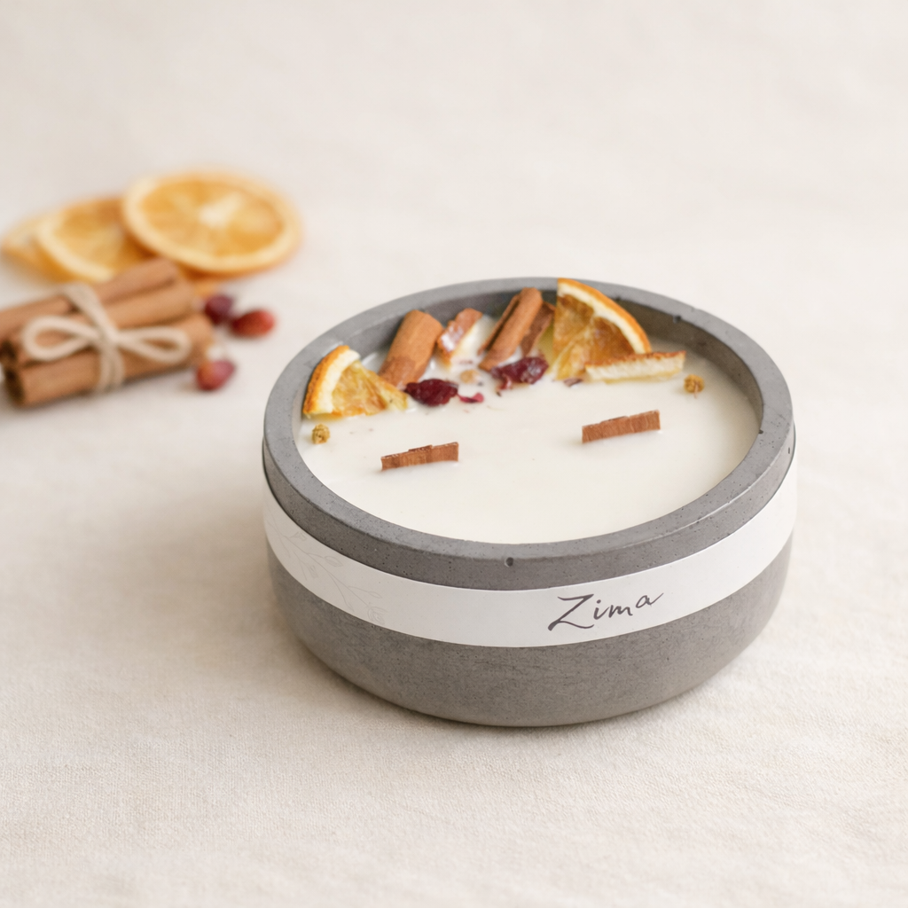 Ručně vyráběná svíčka Zima v matné betonové misce s krémovým voskem, zdobená sušeným pomerančem, skořicí a brusinkami, naaranžovaná v minimalistickém přírodním stylu na světlém béžovém pozadí s měkkým denním světlem.