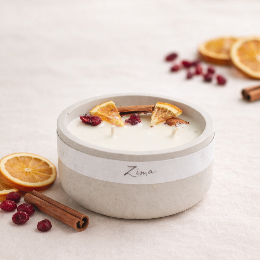 Ručně vyráběná přírodní svíčka v matné světlé keramické nádobě s nápisem Zima, zdobená sušeným pomerančem, brusinkami a skořicí, na světlém krémovém pozadí s jemně rozostřenými přírodními doplňky.