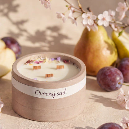 Ručně vyráběná svíčka v keramické misce s květy na vosku, obklopená hruškou, švestkou a rozkvetlými třešňovými květy.