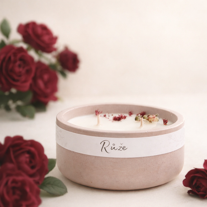 Sójová svíčka s vůní růže v starorůžovém betonovém kalíšku, ruční výroba, doplněná tmavě vínovými růžemi na světlém přírodním pozadí.