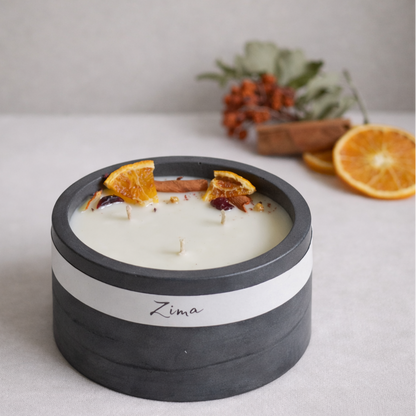 Sójová svicka v betonu se tremi bavlnenymi  knoty s vuni zimy. Zdobena zimnim korenim a pomerancem. V pozadi svicka hori