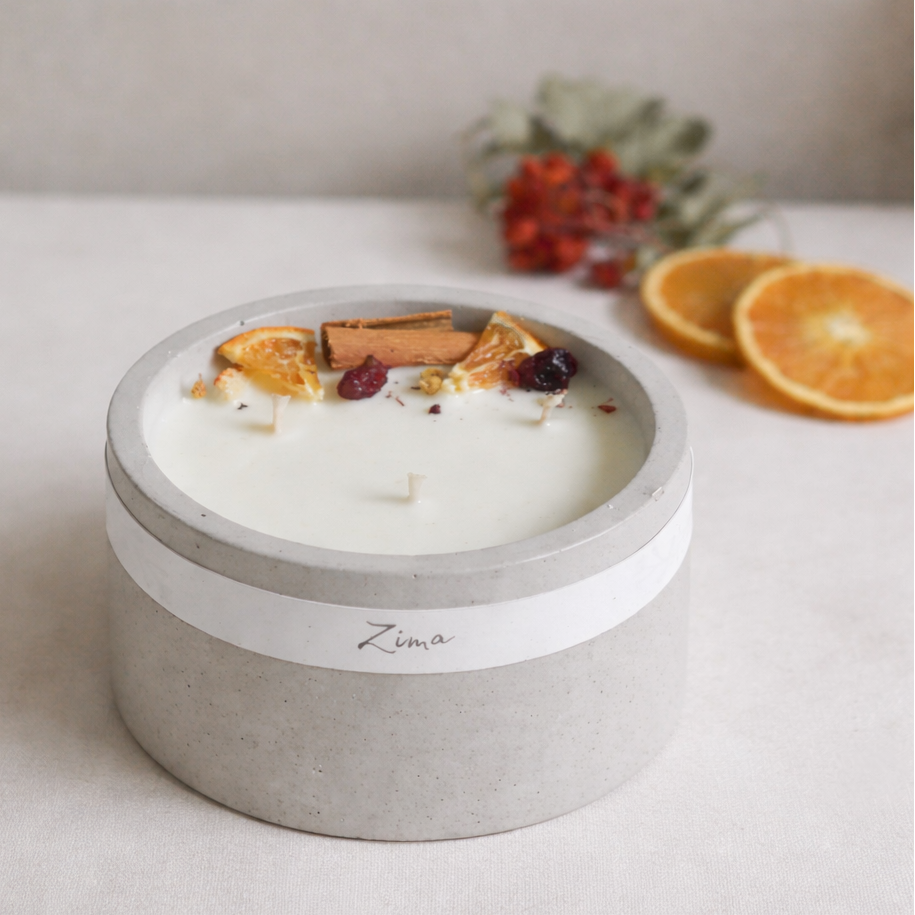 Sójová svicka v betonu se tremi bavlnenymi knoty  s vuni zimy. Zdobena zimnim korenim a pomerancem. V pozadi svicka hori