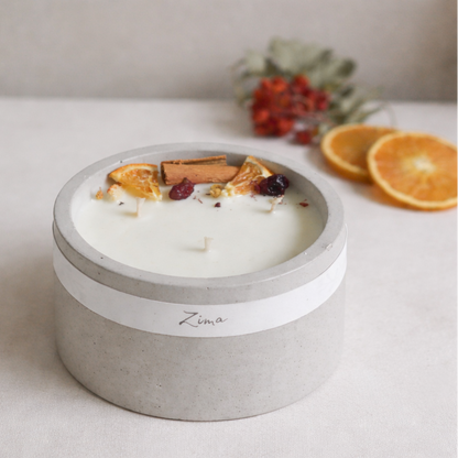 Sójová svicka v betonu se tremi bavlnenymi knoty  s vuni zimy. Zdobena zimnim korenim a pomerancem. V pozadi svicka hori