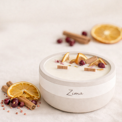 Minimalistická přírodní svíčka Zima v matné keramické dóze na světlém béžovém pozadí, zdobená sušeným pomerančem, brusinkami a skořicí. V popředí i pozadí jemné přírodní dekorace, měkké teplé světlo a klidná, hřejivá atmosféra.