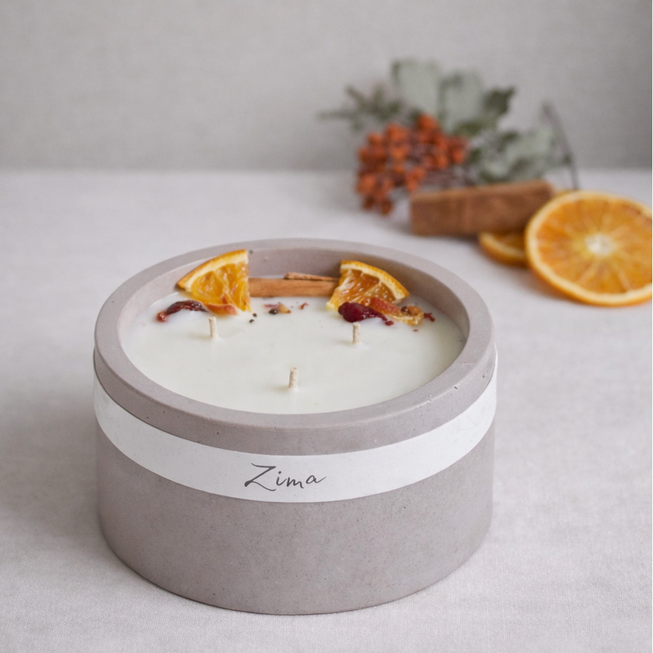 Sójová svicka v betonu se tremi bavlnenymi knoty s vuni zimy. Zdobena zimnim korenim a pomerancem. v pozadi rozostrene zdobeni