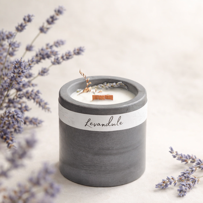 Sojová svíčka s vůní levandule v tmavém betonovém kalíšku, obklopená sušenými květy levandule na světlém přírodním pozadí.