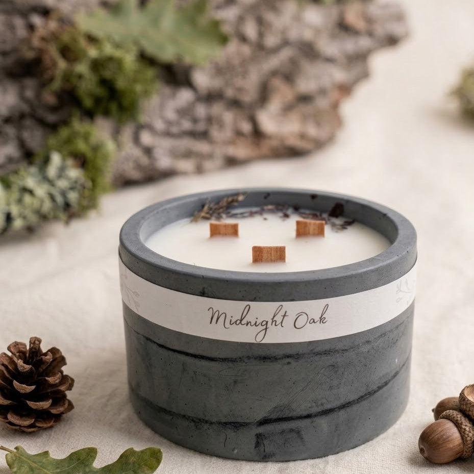 Ručně vyráběná svíčka Midnight Oak v šedé betonové nádobě se třemi dřevěnými knoty, zdobená sušenými botanikami a žaludy.