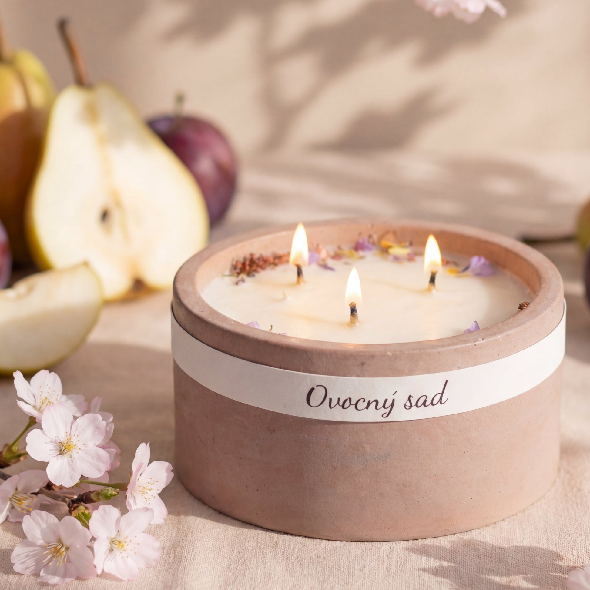 Ručně vyráběná svíčka v keramické misce s květy na vosku, obklopená hruškou, švestkou a rozkvetlými třešňovými květy.