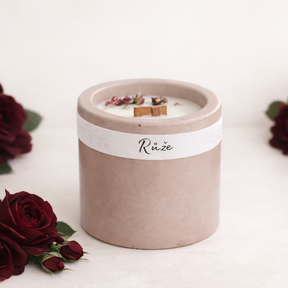 Sójová svíčka s vůní růže v starorůžovém betonovém kalíšku, ruční výroba, doplněná tmavě vínovými růžemi na světlém přírodním pozadí.