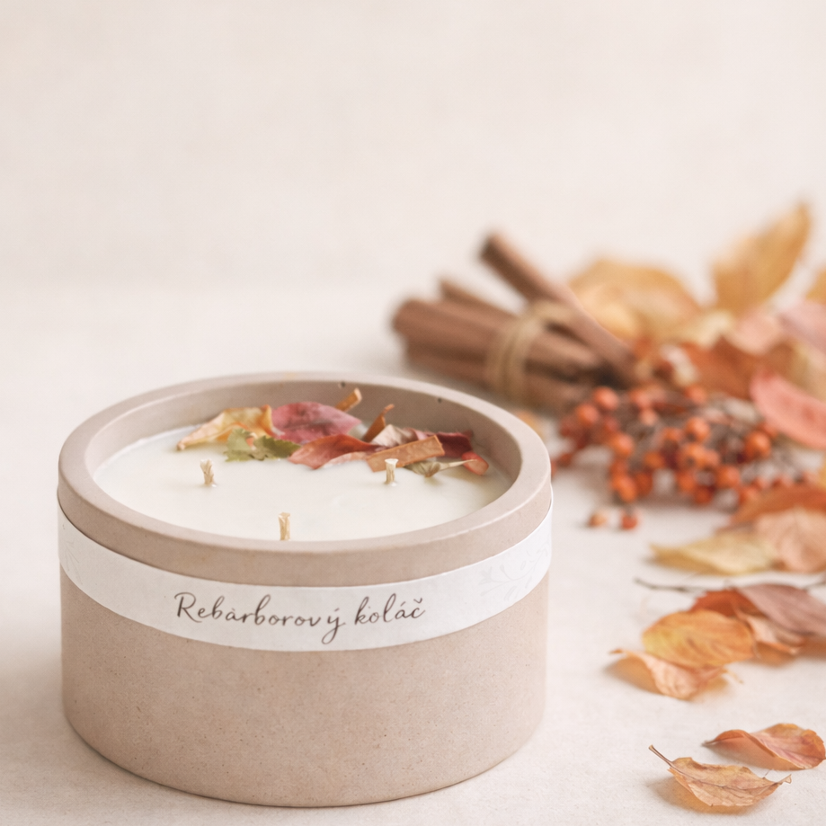 Přírodní ručně vyráběná svíčka v matné keramické dóze s bílým voskem a sušenými květy, aranžovaná v minimalistickém podzimním stylu s listím, skořicí a sušenými jeřabinami na světlém neutrálním pozadí.